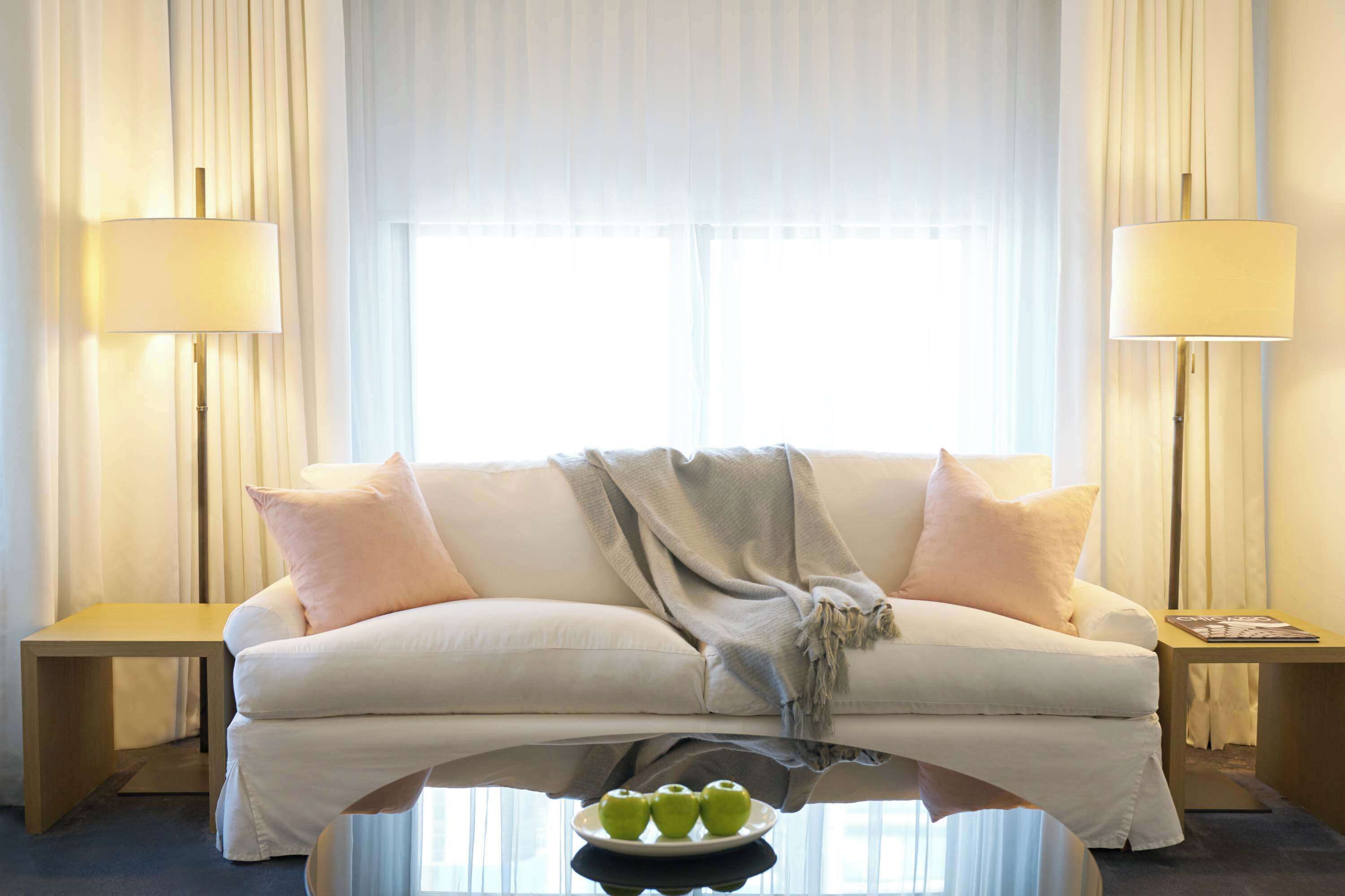 Una sala de estar moderna con un sofá blanco, dos mesas auxiliares y una mesa de centro de vidrio con manzanas verdes.