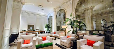 A spacious lobby with high ceilings, large arched windows, and a grand staircase.
