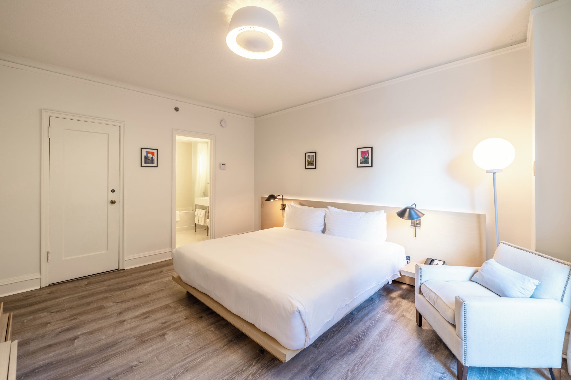 A hotel room with a large bed, bedside tables, a desk, a chair, and a bathroom visible through an open door.