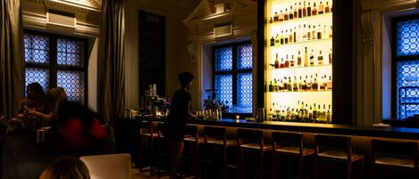 A bar area with a large illuminated liquor display, seating, and a person standing by the bar.