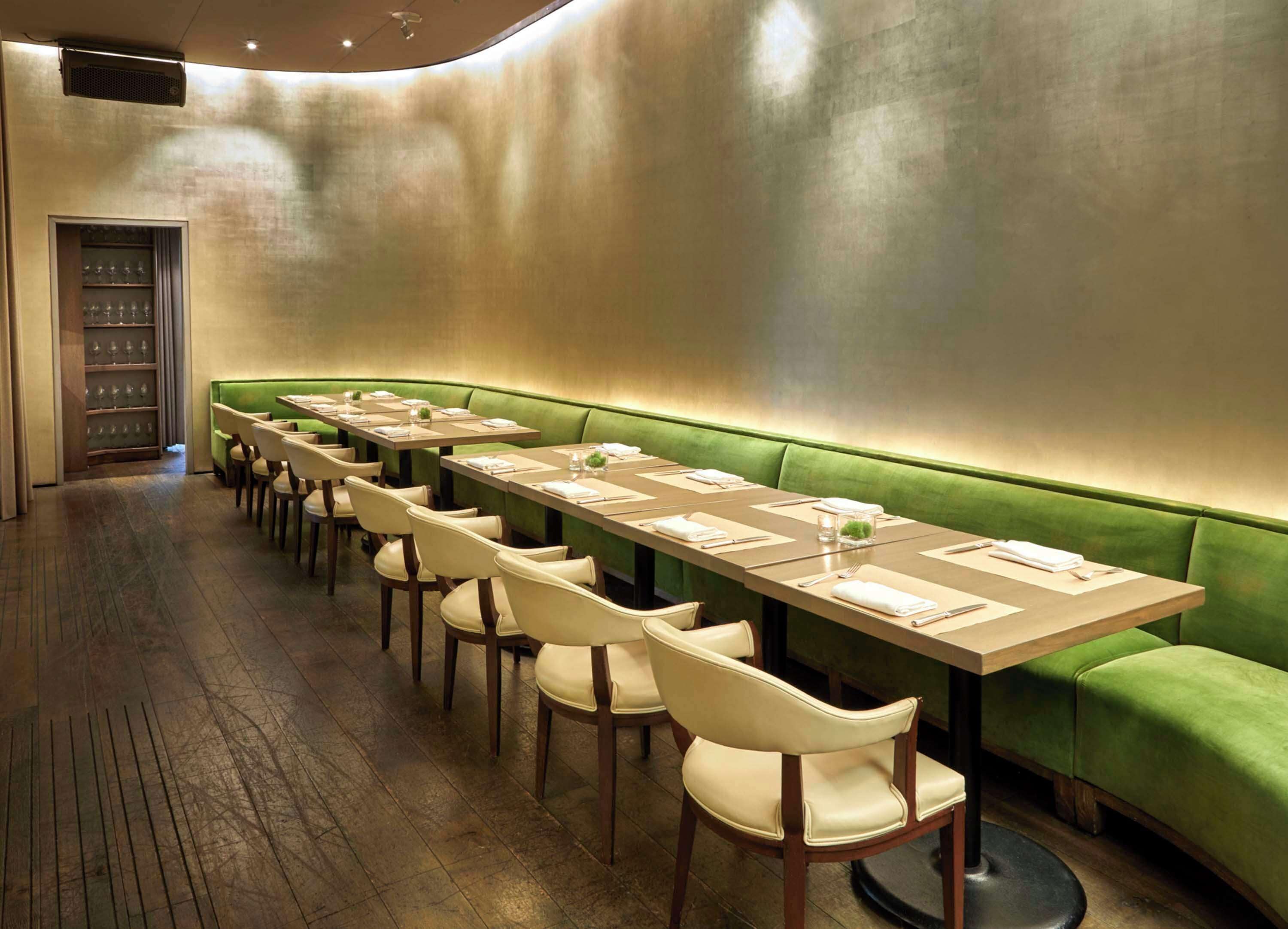 A restaurant with long tables, green upholstered booths, and wooden flooring.