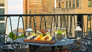Un balcon avec une table dressée pour un repas, agrémentée d’une planche de charcuterie et de deux verres de vin, offrant une vue sur le paysage urbain.