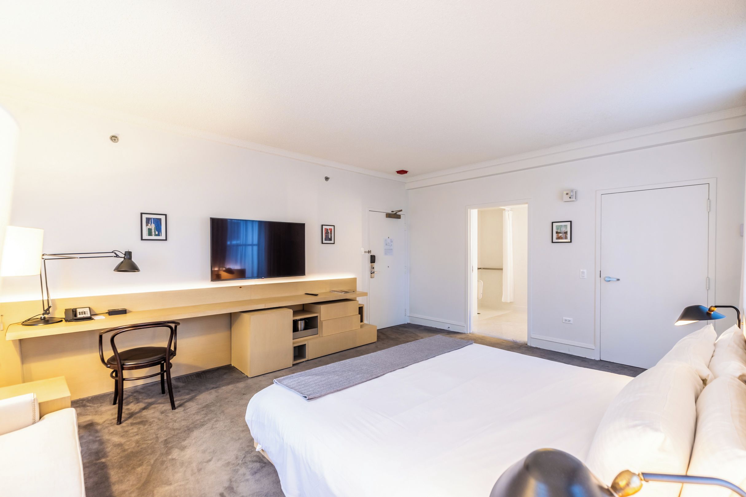 A hotel room with a bed, a desk with a computer, a chair, a television, and a door.