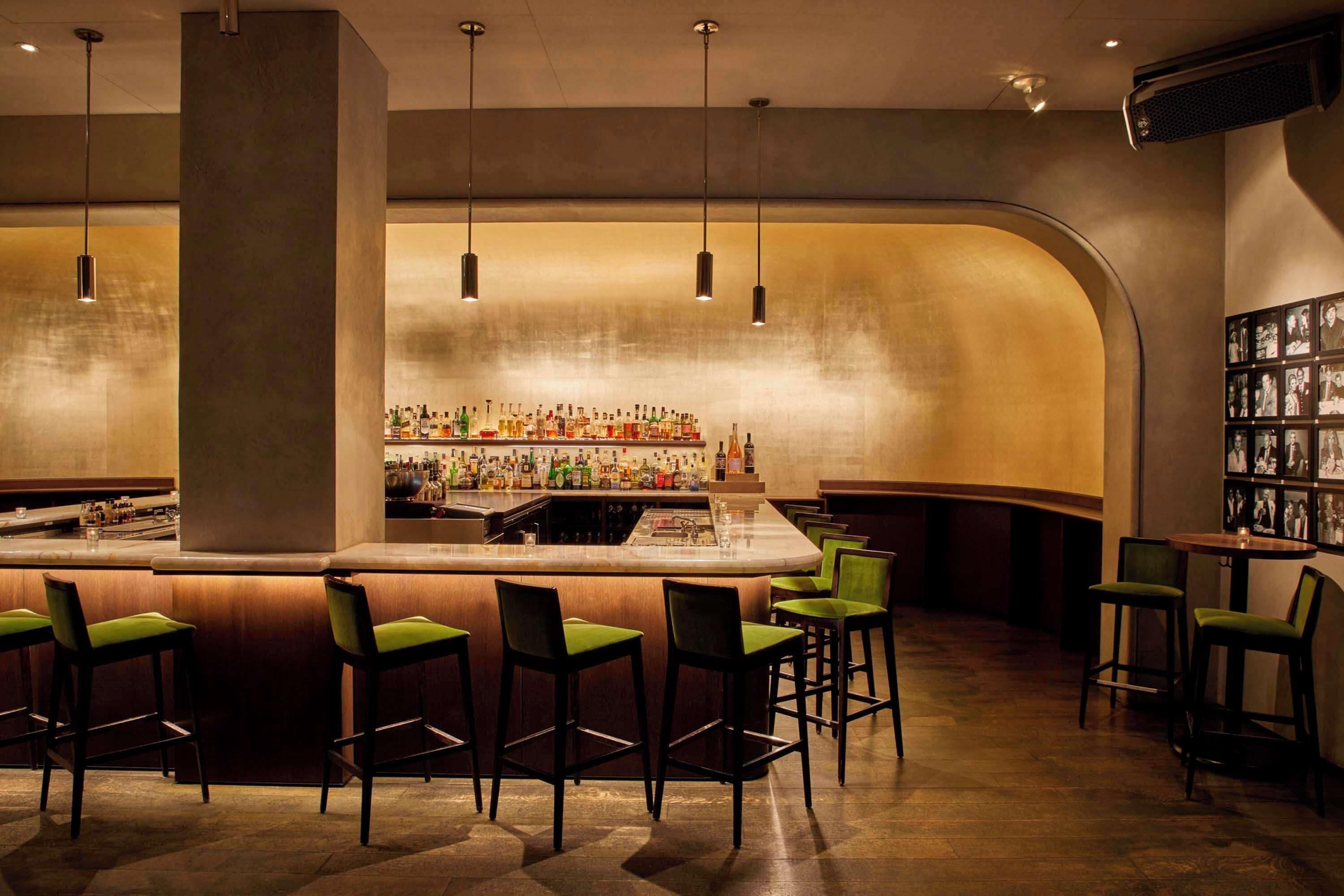 A bar area with a curved counter, multiple hanging pendant lights, and bar stools with green cushions.