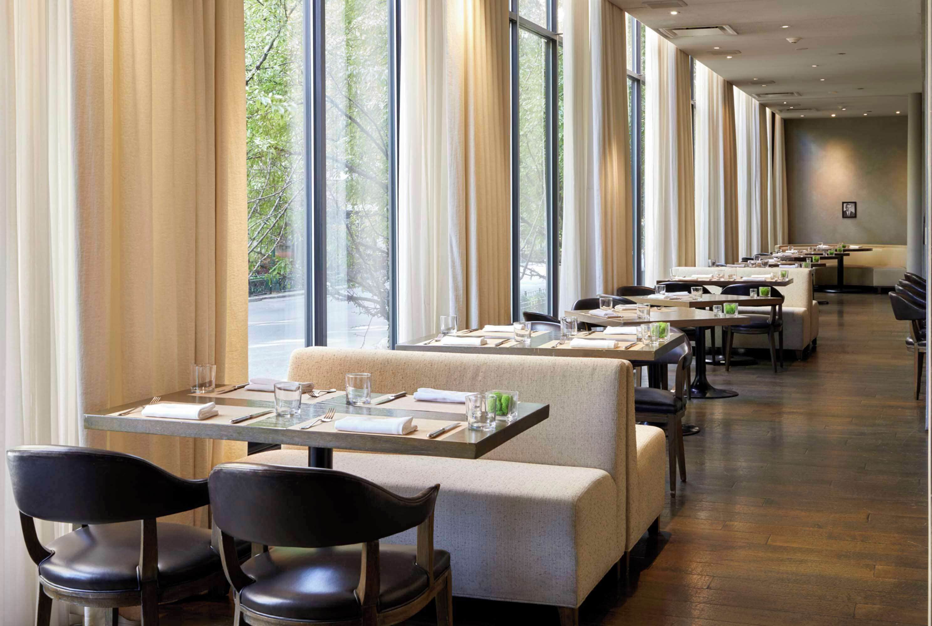 Un restaurante con varias mesas y cabinas, ventanas amplias con cortinas y suelo de madera.