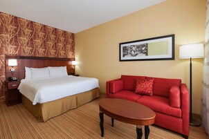 A hotel room with a bed, a red sofa, a small table, a framed picture on the wall, and a lamp.