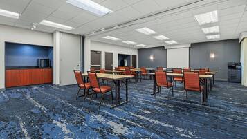 A conference room with multiple tables and chairs, a television, and a kitchenette area.