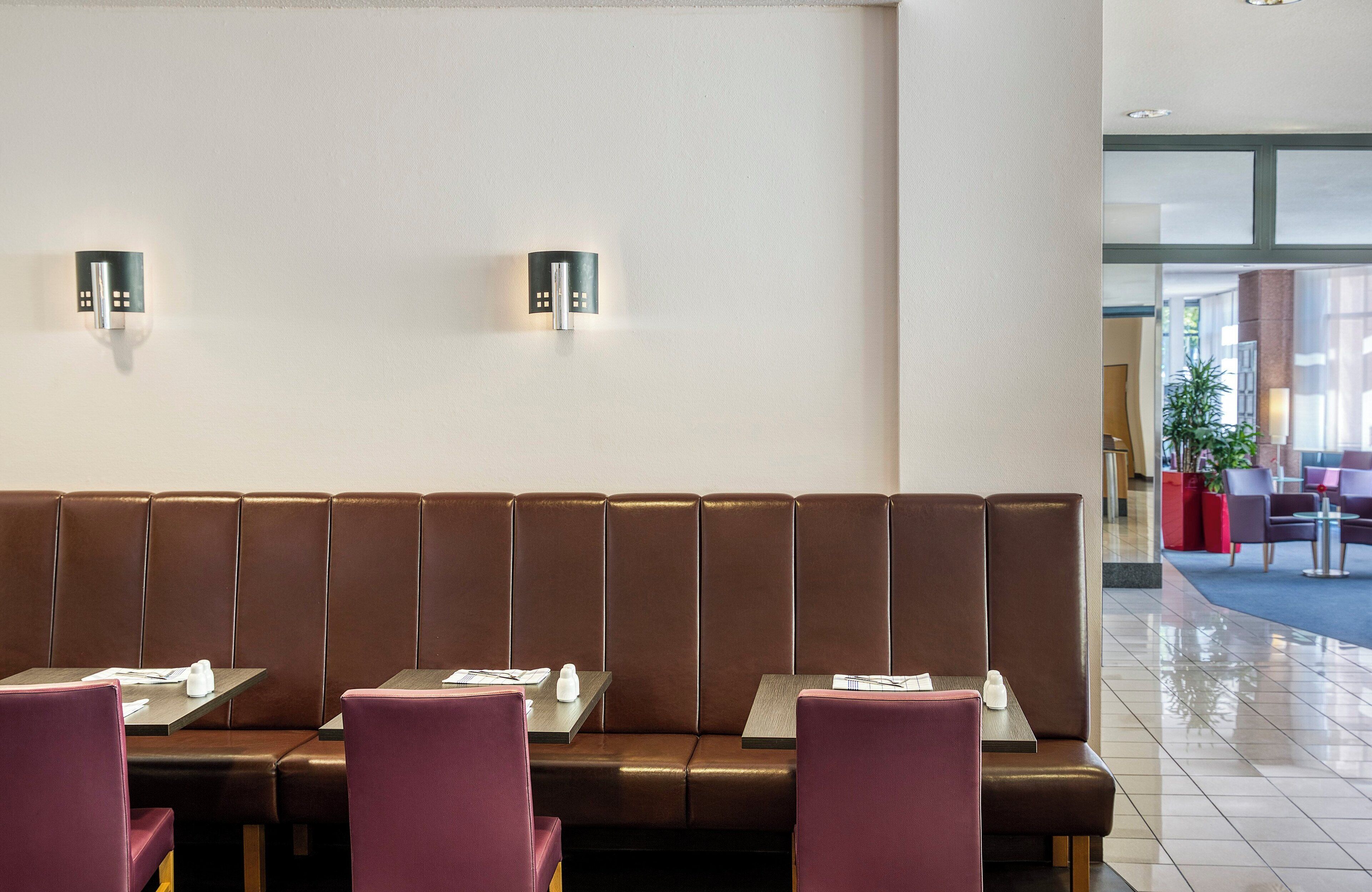 Un restaurante moderno con asientos de cuero marrón y sillas moradas. Hay dos lámparas fijadas a la pared. Las mesas tienen menús y condimentos. El interior es limpio y bien iluminado.