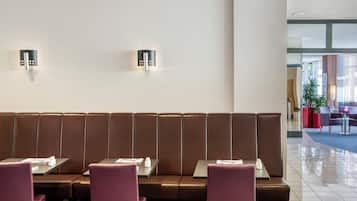 Un restaurante moderno con asientos de cuero marrón y sillas moradas. Hay dos lámparas fijadas a la pared. Las mesas tienen menús y condimentos. El interior es limpio y bien iluminado.