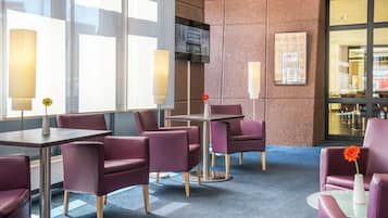 En modern hotellobby med lila sittmöbler, ett glasbord och ett stort fönster.