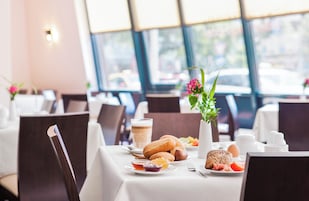 Una mesa de comedor con alimentos para el desayuno, incluyendo pan, huevos y una bebida de café, en una habitación luminosa con ventanas amplias.