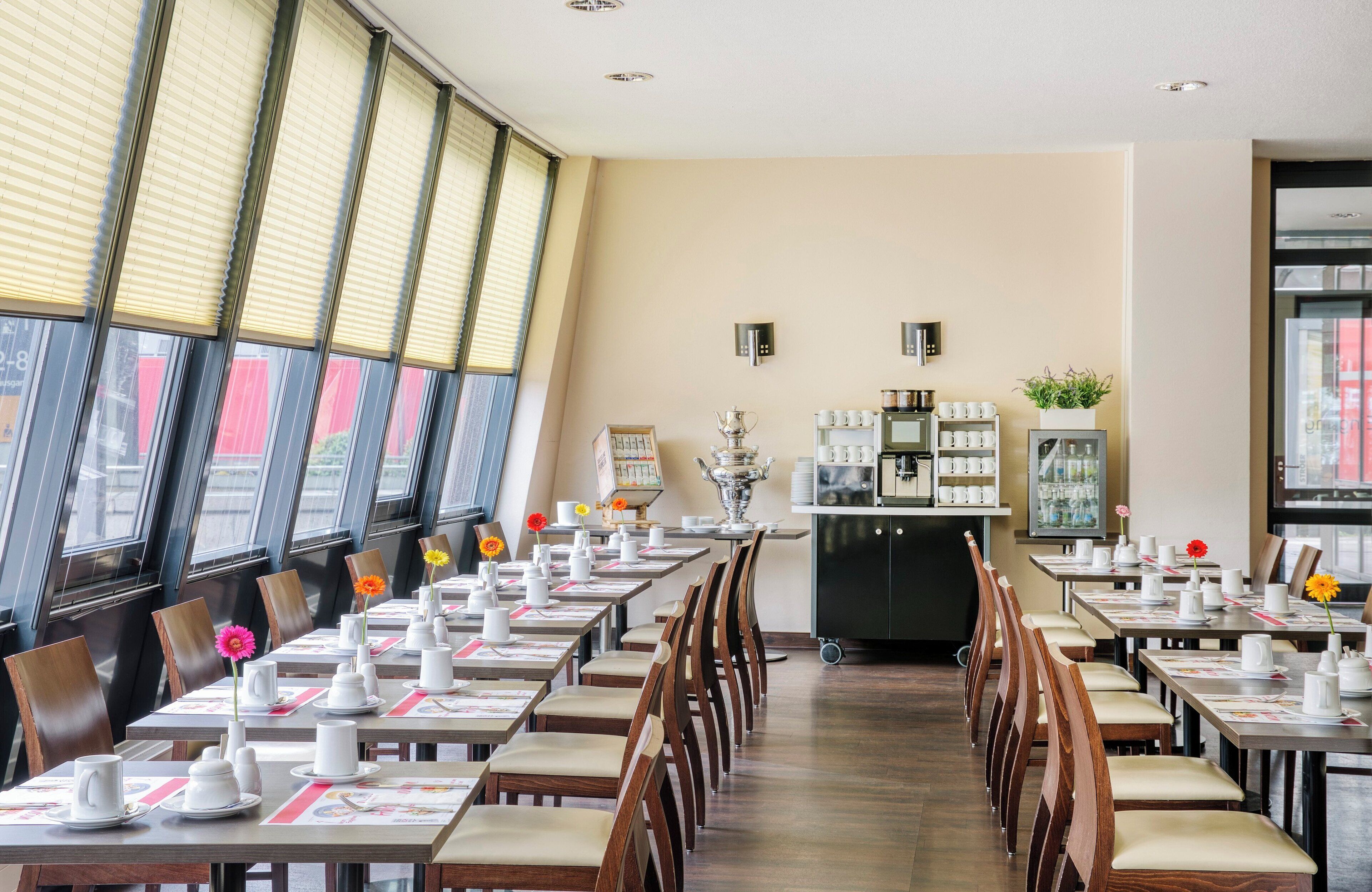 Un restaurante con mesas largas dispuestas para comer, una estación de café y vistas a través de amplios ventanales.