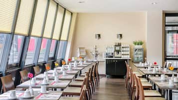 A restaurant with long tables set for dining, a coffee station, and a view through large windows.