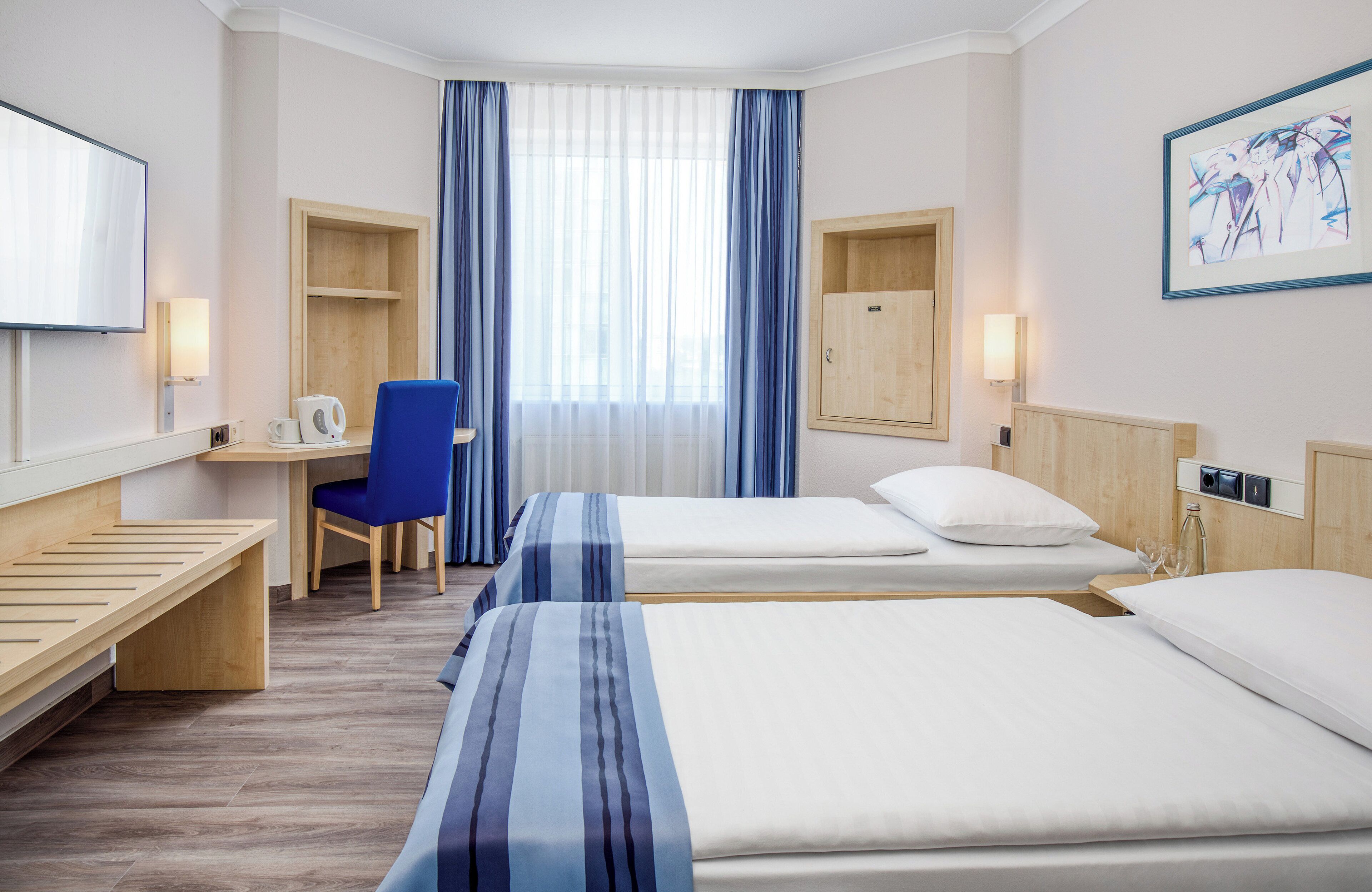 A hotel room with two beds, a desk with a chair, a TV, and a window with curtains.