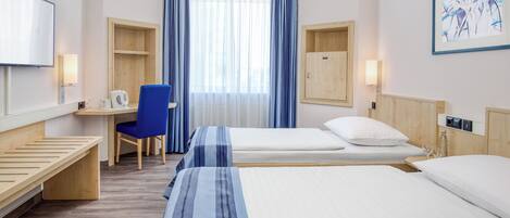Habitación de hotel con dos camas, un escritorio con silla, televisión y ventana con cortinas.