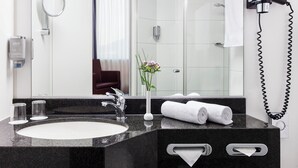Un baño moderno con encimera de granito, un lavabo, un espejo, toallero, secador de pelo y un florero con flores.