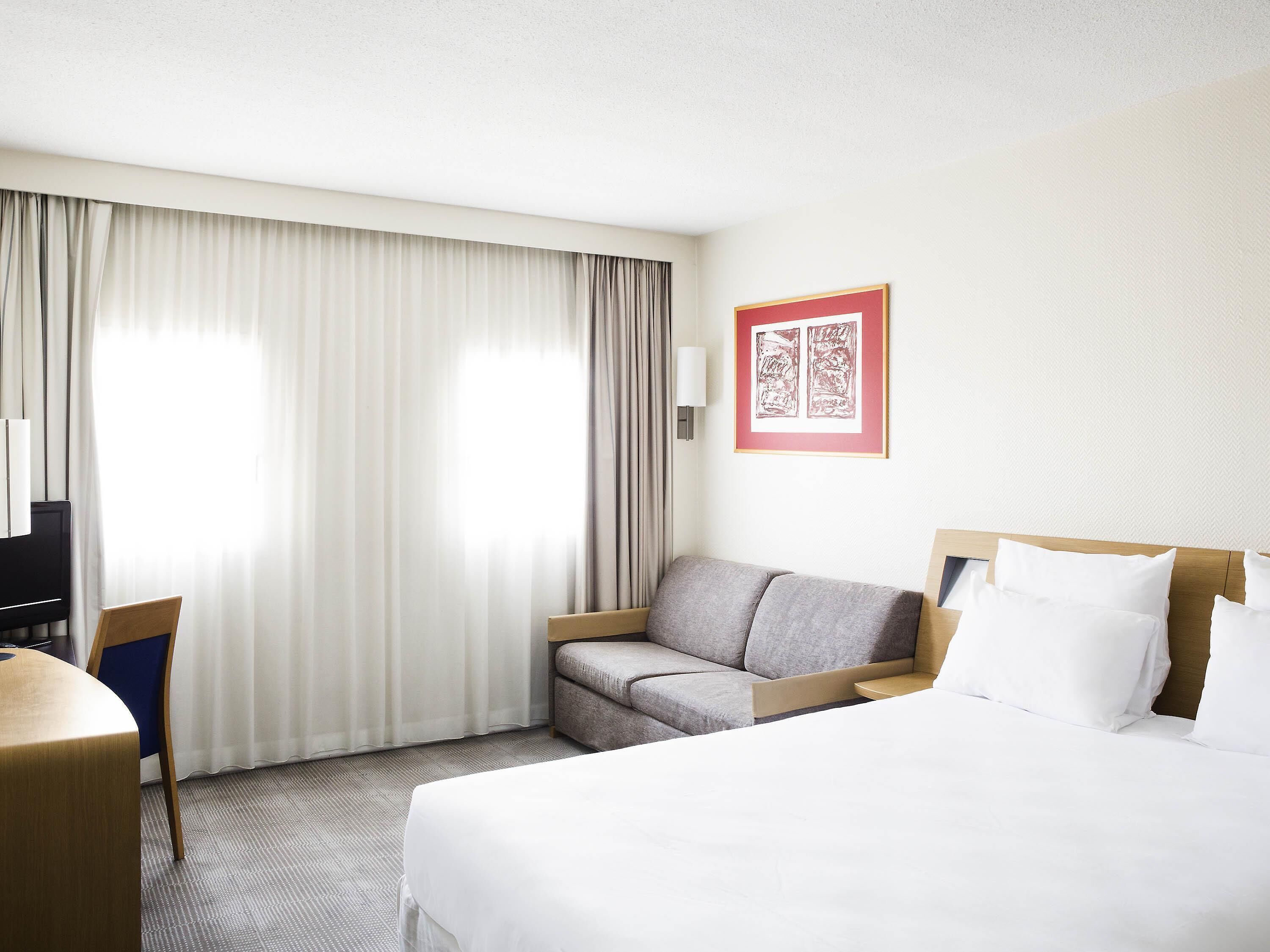 A hotel room with a bed, a sofa, a desk, and a chair.
