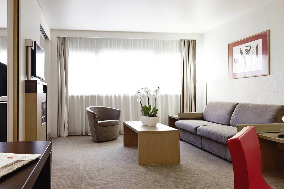 Een moderne hotelkamer met een bank, fauteuil, salontafel en een televisie.