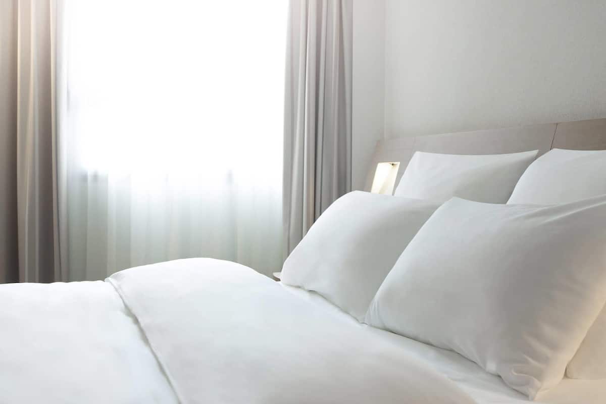 Une chambre d’hôtel avec un lit bien fait, une tête de lit et des rideaux légers.