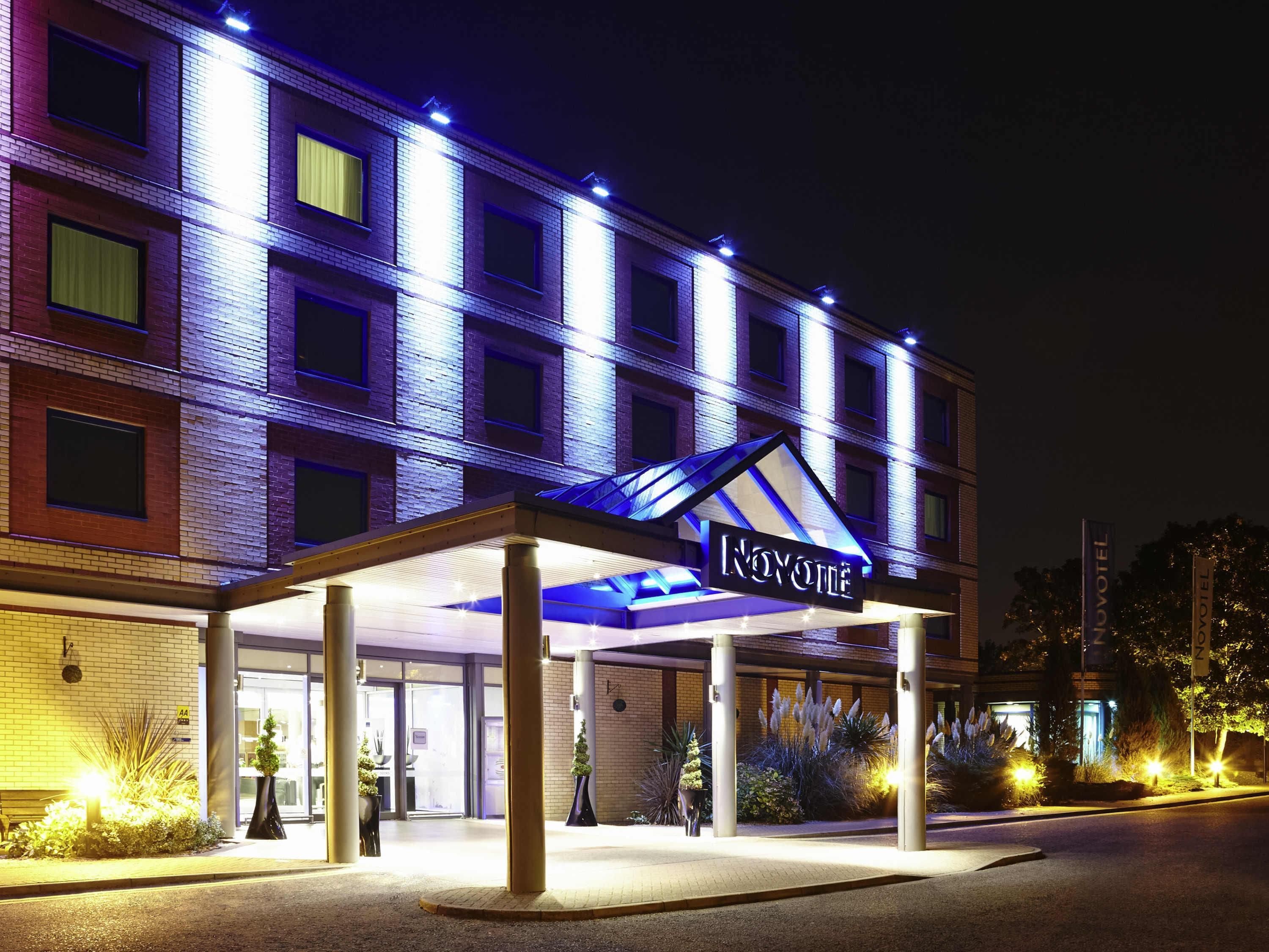 A hotel entrance with a covered walkway, a sign reading 'NOVOMILE,' and a brick facade.