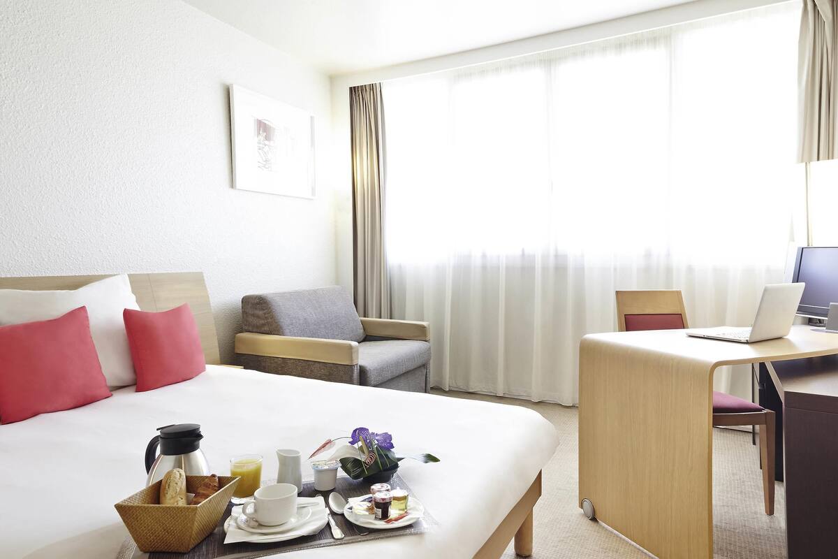 Hotelkamer met een bed, een bureau met een laptop, een stoel en een ontbijtserver met koffie, sap en gebak.