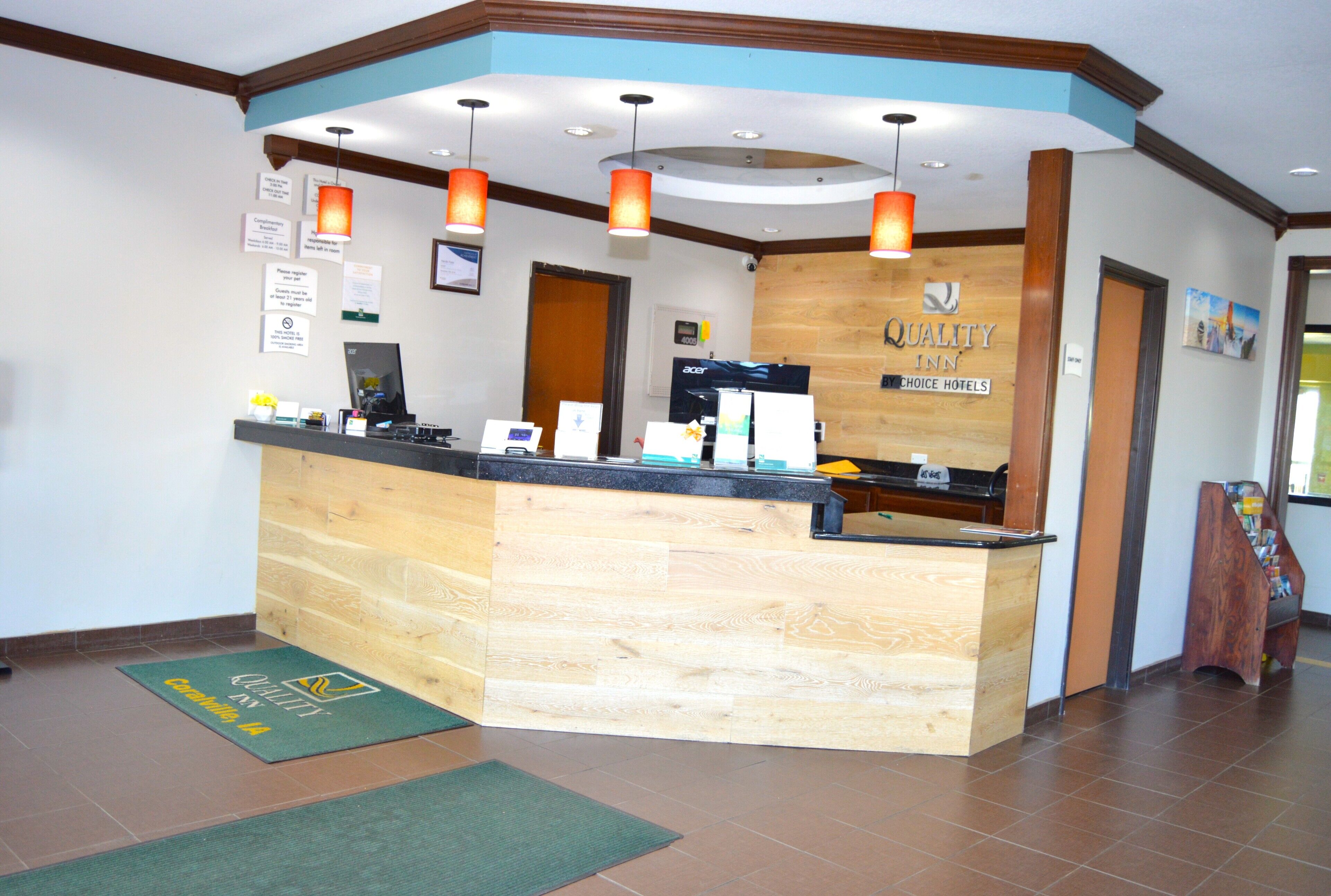 A reception desk with a wooden finish, a digital screen, and a sign indicating it's a Quality Inn by Choice Hotels.