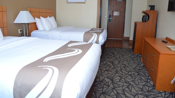 A hotel room with two beds, a desk, a lamp, a door, and a framed picture on the wall. - Quality Inn Coralville - Iowa River Landing (Coralville)