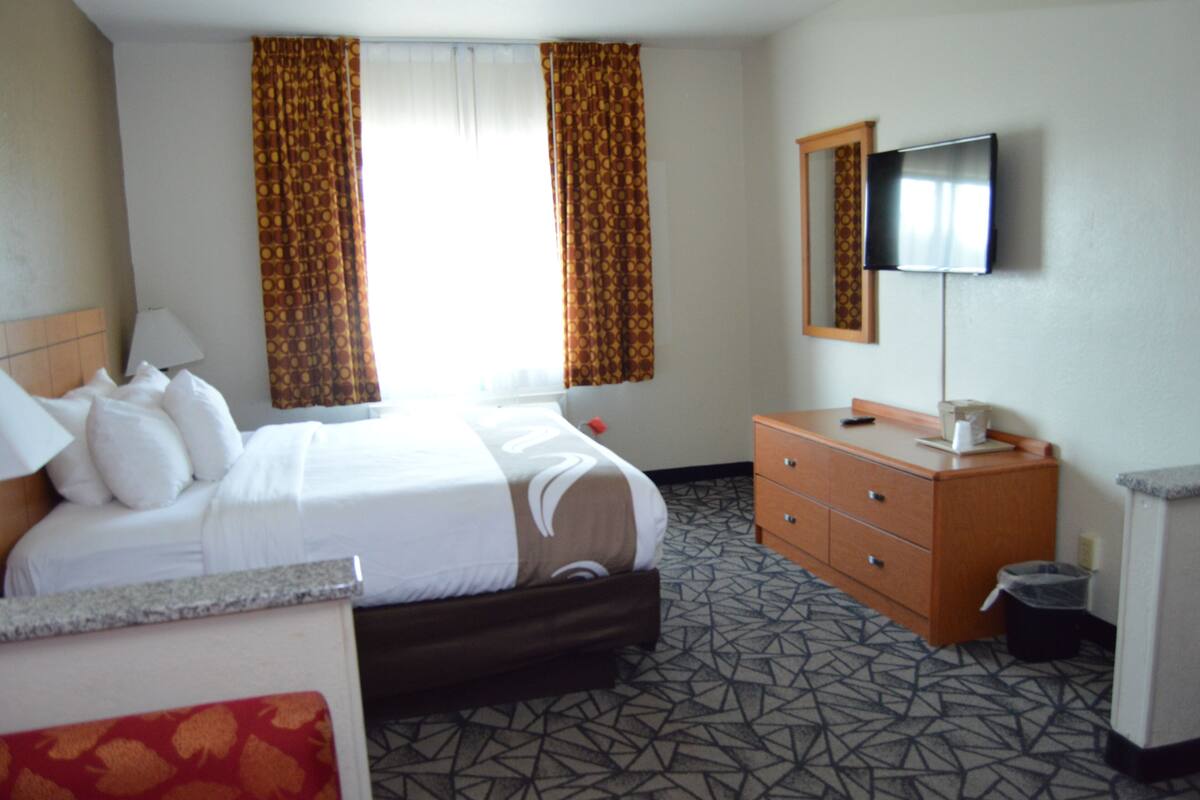 A hotel room with a bed, a dresser, a television, and a window with curtains.
