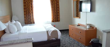 A hotel room with a bed, a dresser, a television, and a window with curtains.