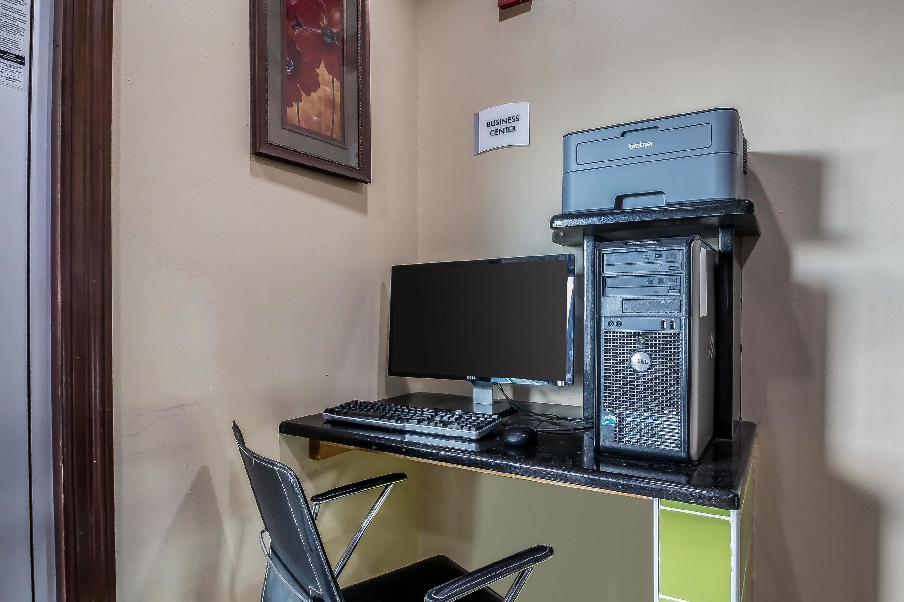 A business center desk with a desktop computer, a monitor, a keyboard, a mouse, and a printer.