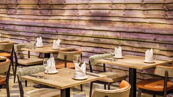 Een restaurant met houten wanden, tafels met witte servetten en rieten stoelen.
