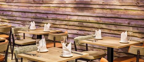 A restaurant with wooden walls, tables with white napkins, and wicker chairs.