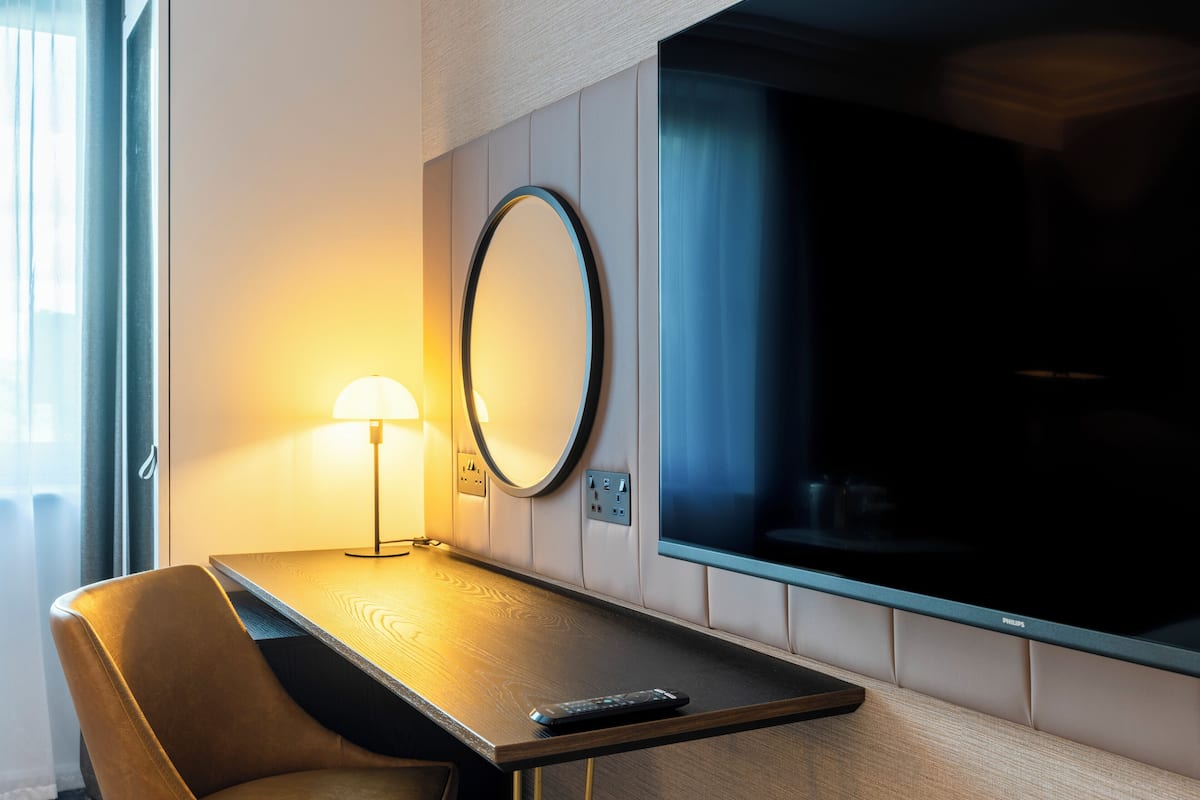 Une chambre d’hôtel avec un bureau en bois, un miroir rond, une lampe et un téléviseur.