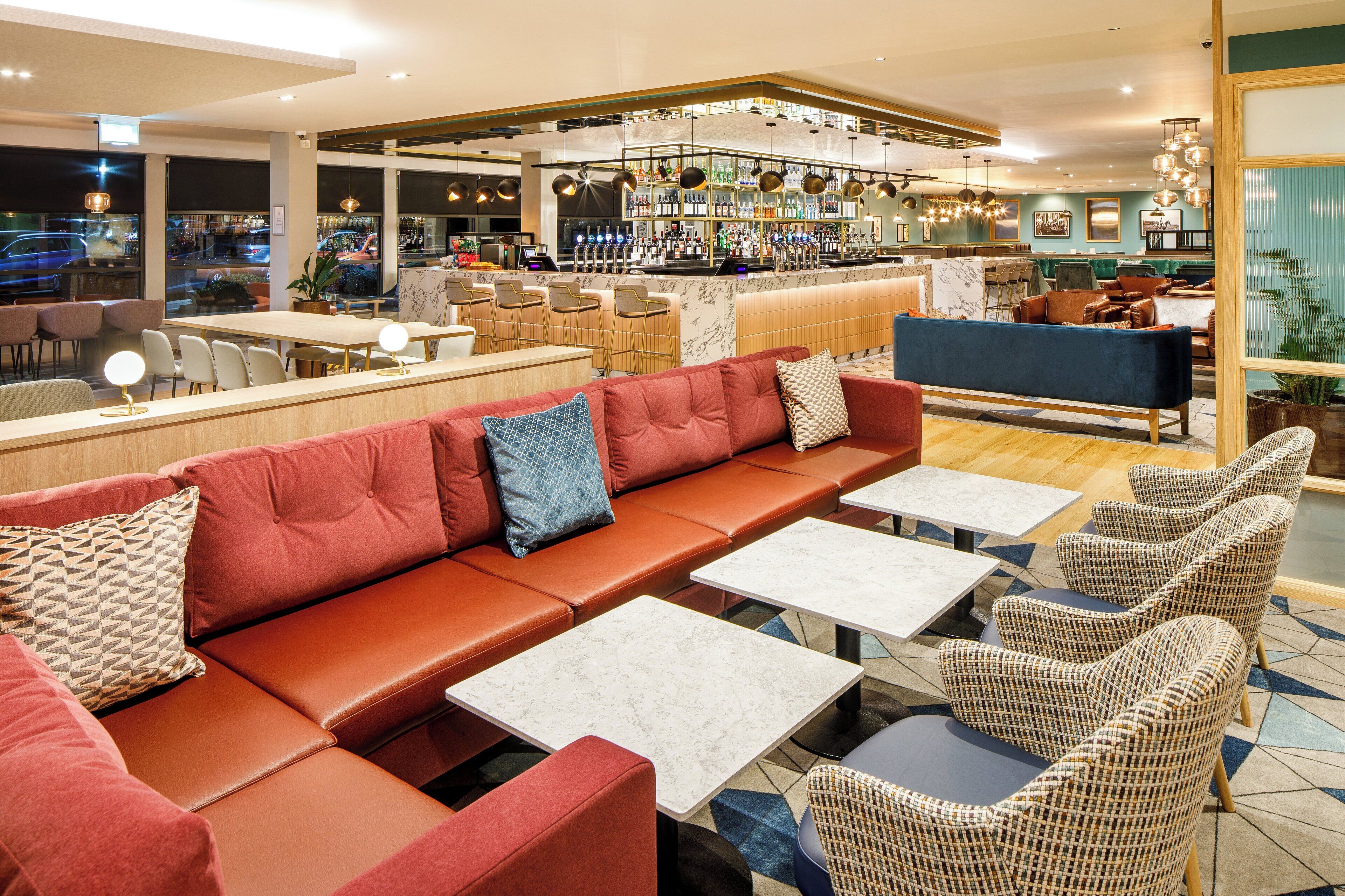 A modern bar area with seating, a bar counter, and a view of the street outside.