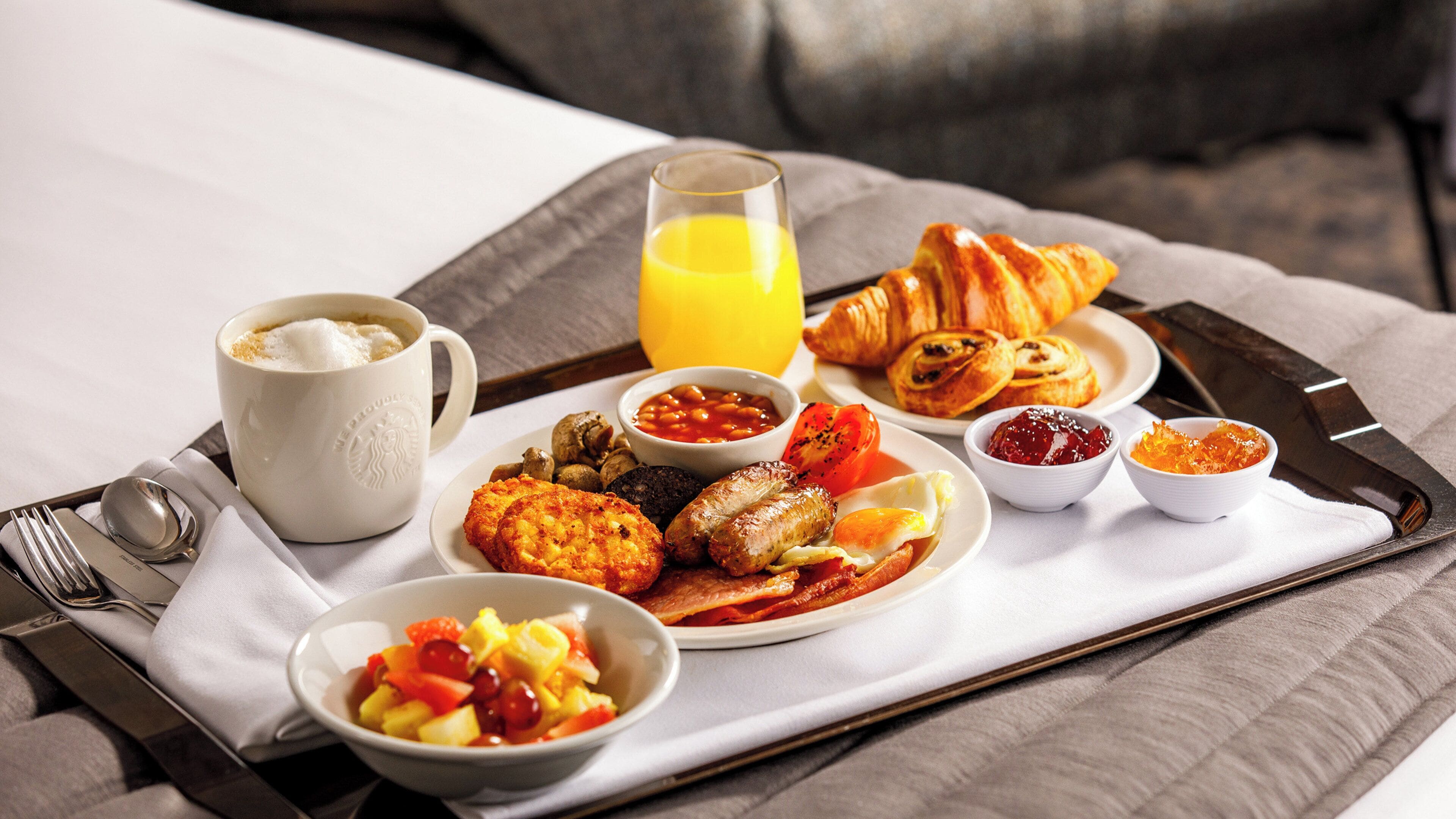 Ein Frühstücksbrett mit Croissants, Würstchen, Eiern, Toast und Obst.