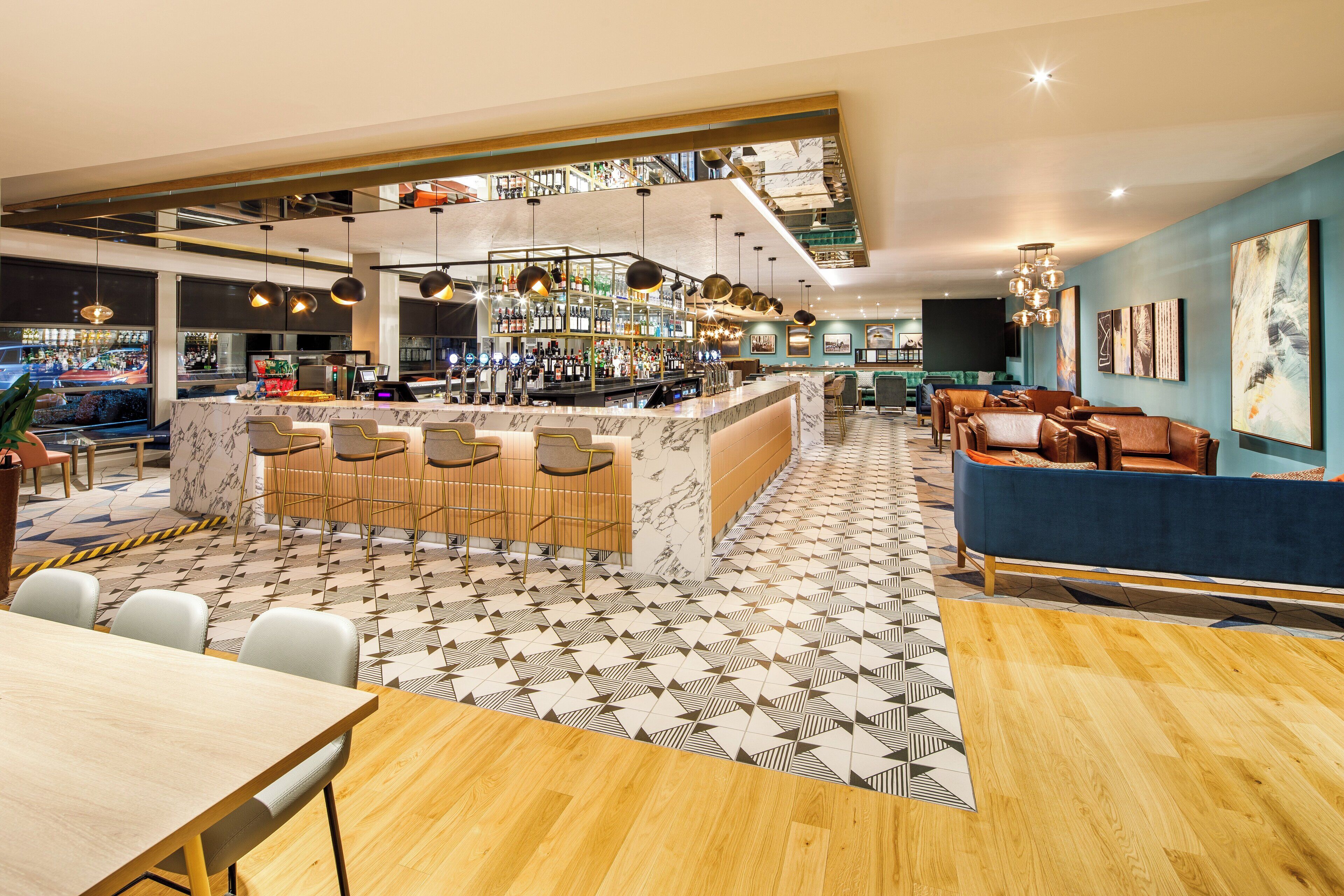A modern bar area with a marble counter, multiple bar stools, and hanging pendant lights.
