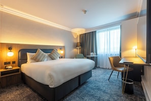Una habitación de hotel con una cama grande, mesitas de noche, un escritorio, una silla y una ventana con cortinas.