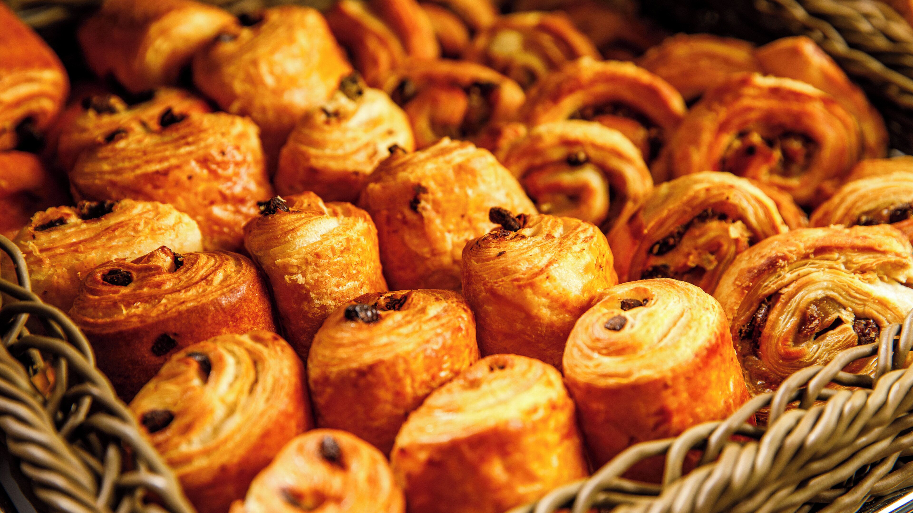 Ein Korb voller verschiedener Backwaren, darunter Croissants und Brötchen, dicht aneinander gereiht.