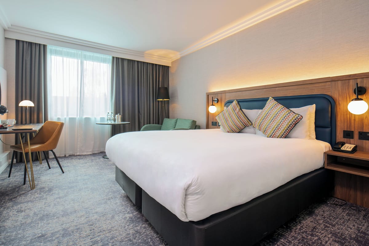 Une chambre d’hôtel avec un grand lit, un bureau, une chaise, une petite table et une lampe.