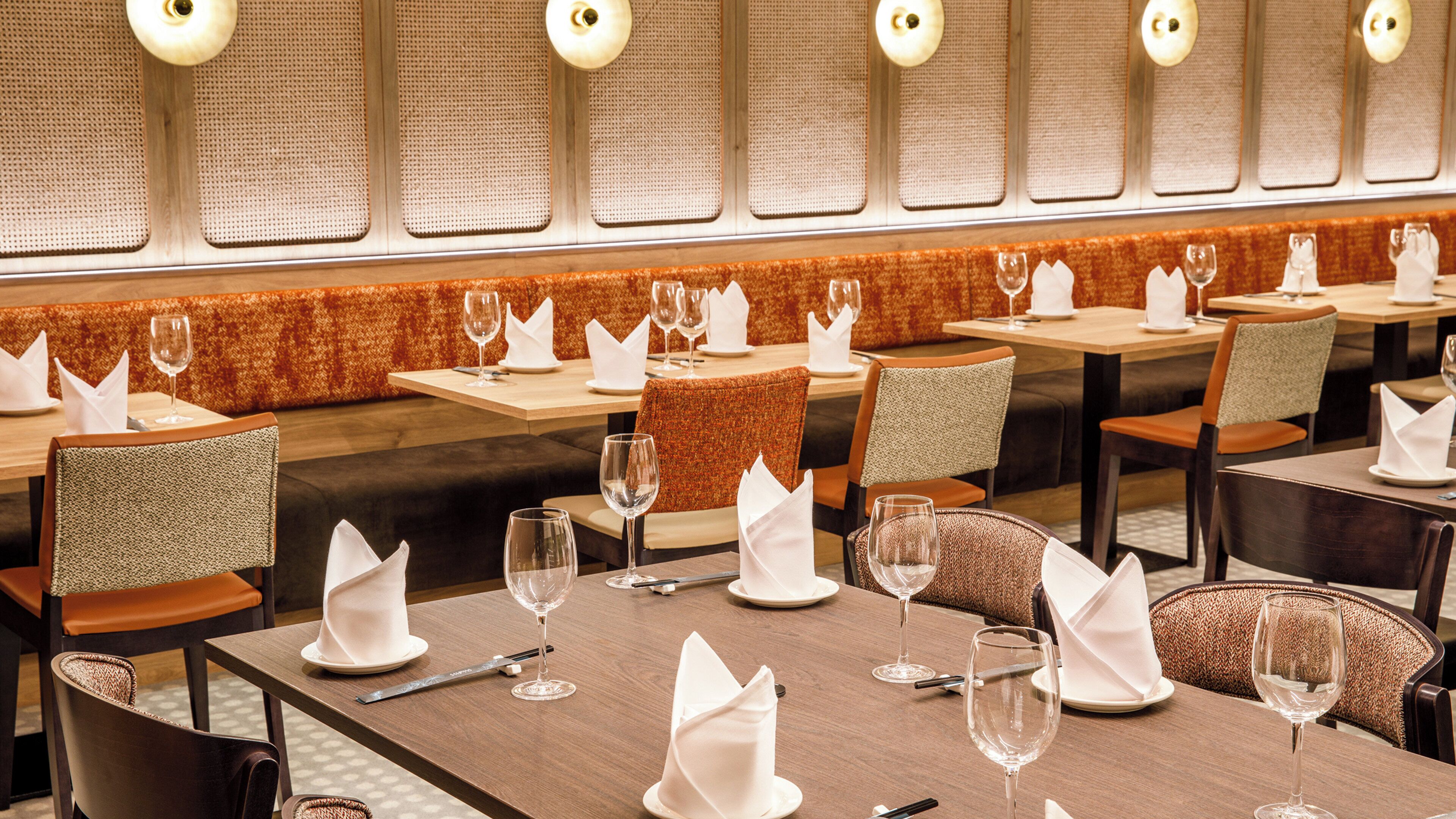 Ein Restaurant mit gedeckten Tischen, einer strukturierten Wand und einer Reihe von Lampen.