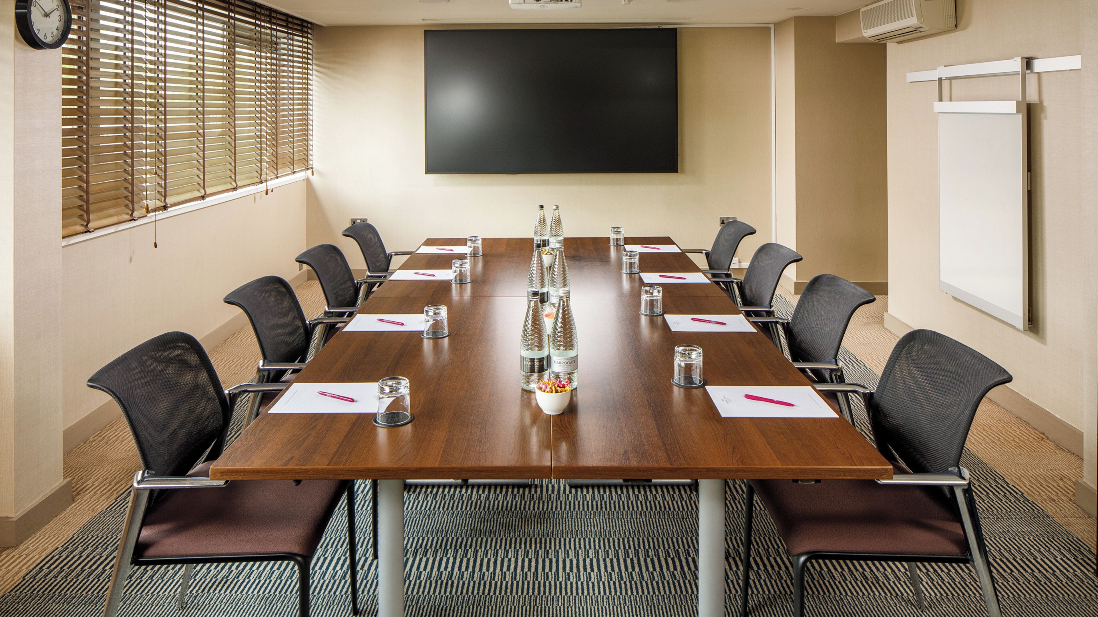 A conference room with a long table, chairs, a projector screen, and a whiteboard.