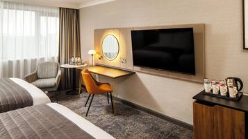 A hotel room with a bed, a desk, a chair, a TV, a coffee maker, and a tray with coffee cups.