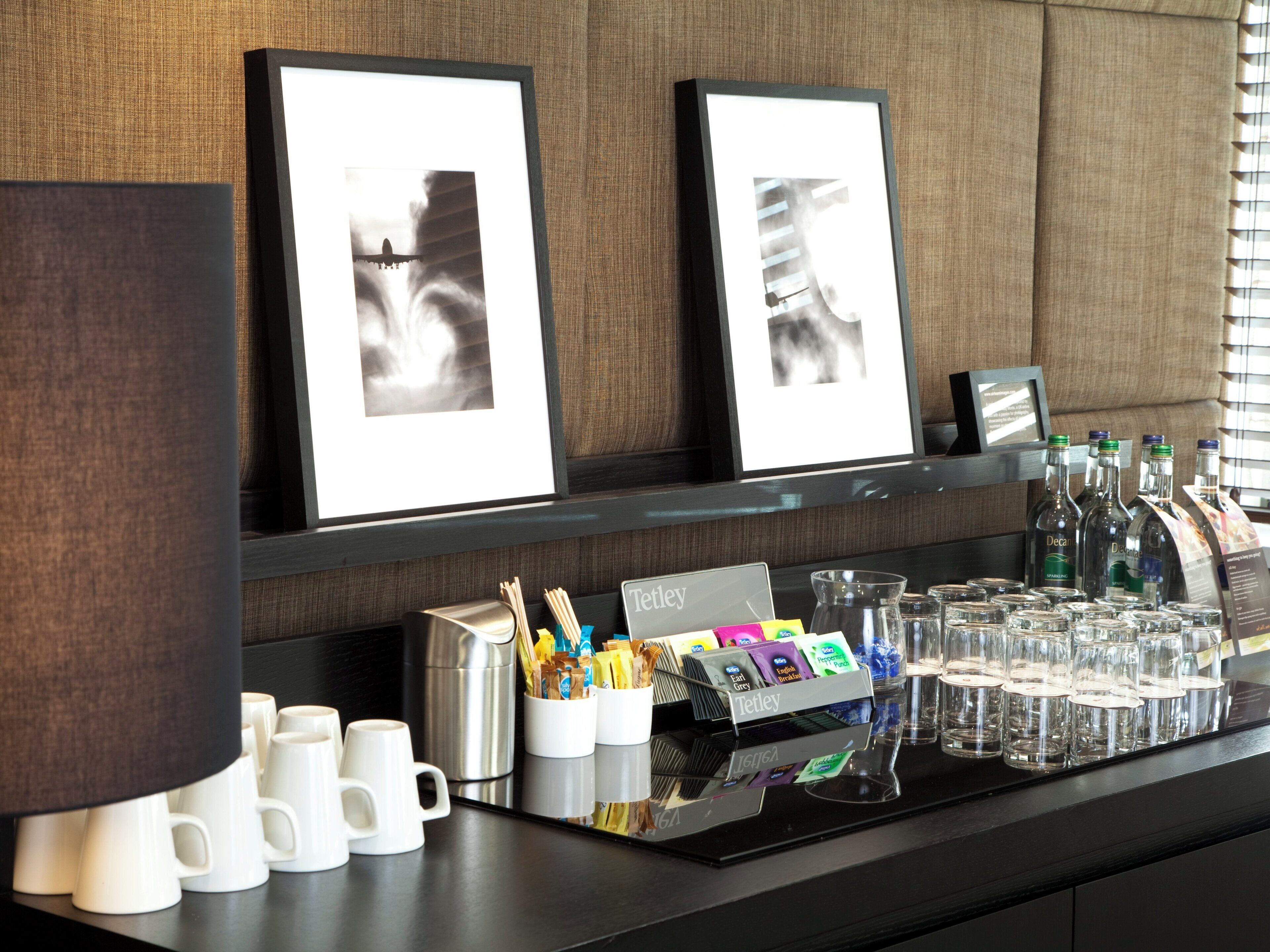 Zona de recepción de un hotel con cuadros enmarcados, una estación de café y una exhibición de bebidas embotelladas.