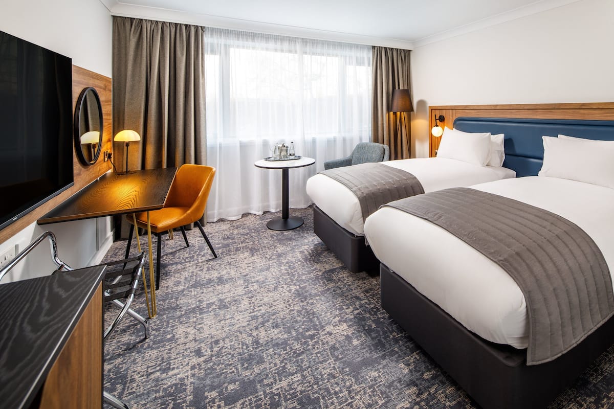 Une chambre d’hôtel avec un grand lit, un bureau avec une chaise, une télévision et une petite table avec une lampe.