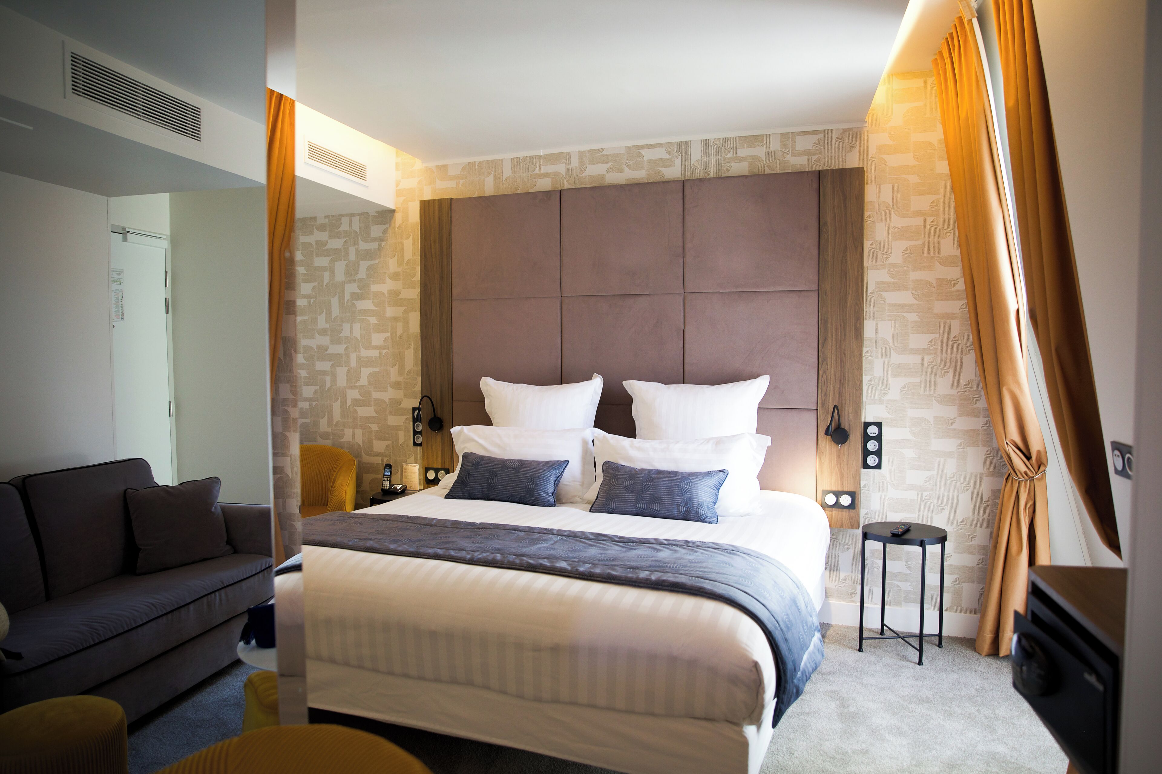 A modern hotel room with a large bed, a sofa, and a small table.