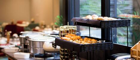 A buffet setup with various food items and a large window in the background.