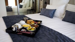 Una cama bien hecha con una bandeja de desayuno que incluye huevos, pan y fruta.