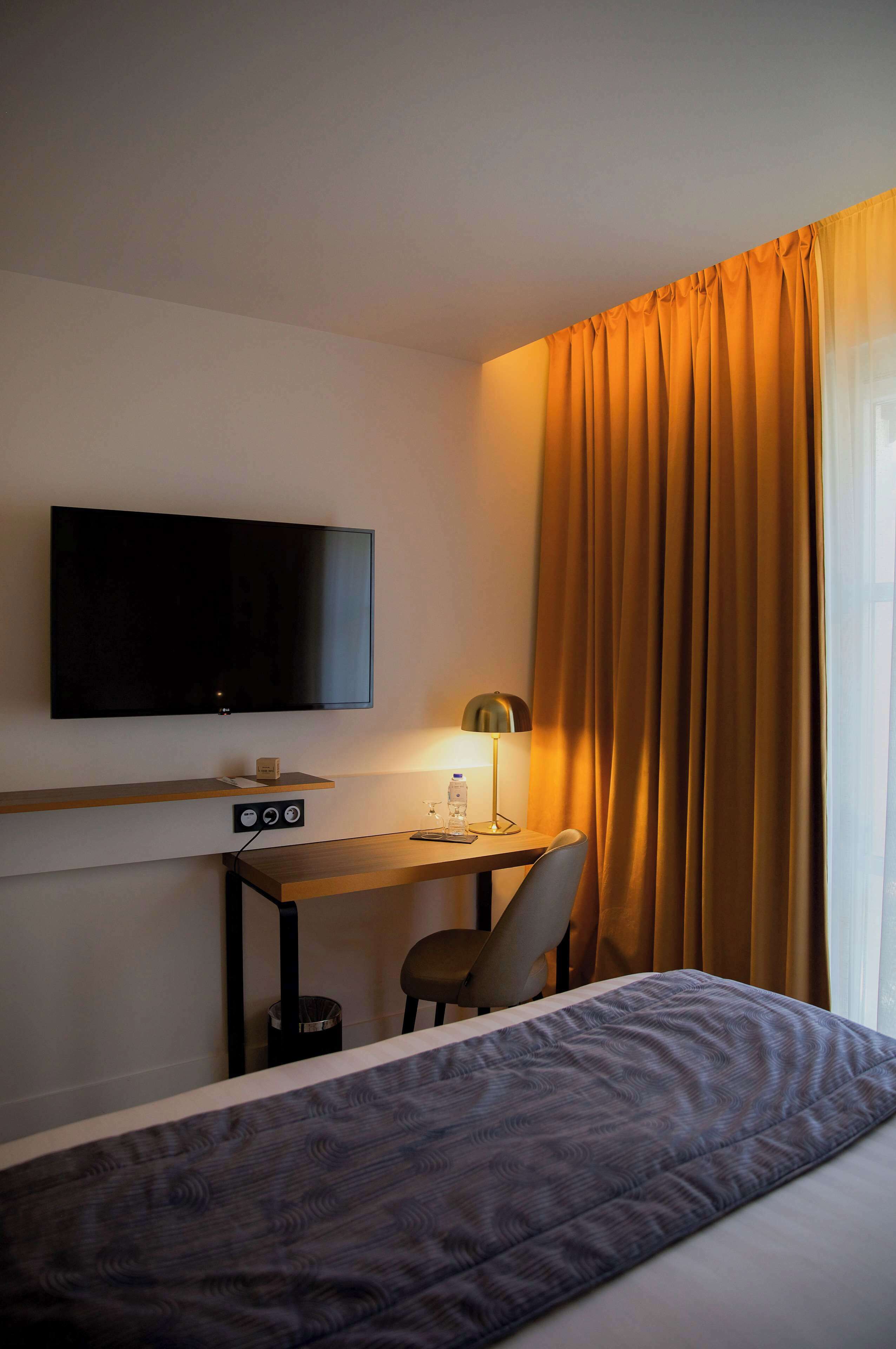 Una habitación de hotel con una cama, un escritorio con televisor, una silla y una lámpara.