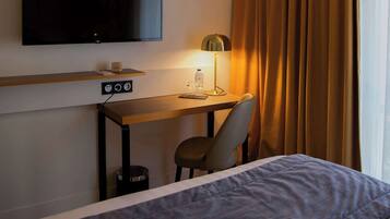 Una habitación de hotel con una cama, un escritorio con televisor, una silla y una lámpara.