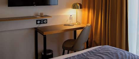Una habitación de hotel con una cama, un escritorio con televisor, una silla y una lámpara.